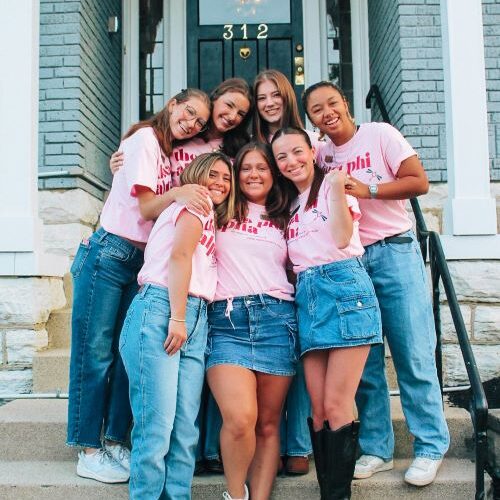 Members in pink standing on steps in front of house