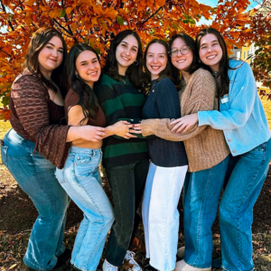 Members hugging and smiling by tree in fall